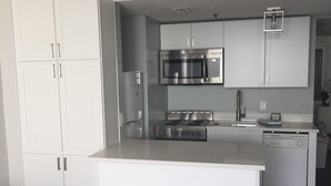 A modern kitchen with white cabinets, stainless steel appliances, and a central island with stools. - Brand New Reno! OF, End Unit, King bed, Quartz Counters, Shaker Cabinets (Myrtle Beach)