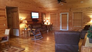 Un interior acogedor de cabaña de troncos con televisor, mecedora y mobiliario de madera.