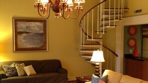 Ein Wohnzimmer mit einer Chandelüster, einer Treppe und einem Gemälde an der Wand.