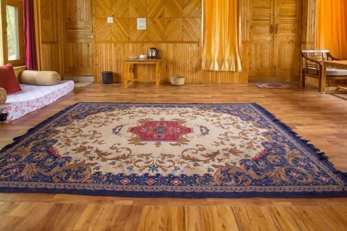 A wooden interior with a large rug, a sofa, a table with a kettle, and a chair.