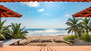 A beach view from a covered area with a wooden floor, palm trees, and a clear sky. - Luxurious Troncones Beachfront! 30mins to Ixtapa (Troncones)