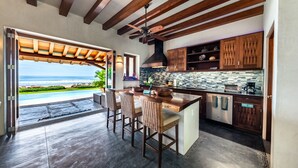 A kitchen with a view of the ocean, wooden ceiling beams, and a bar area with wicker chairs. - Luxurious Troncones Beachfront! 30mins to Ixtapa (Troncones)