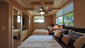 Ein Schlafzimmer mit zwei Betten, einem Deckenventilator, einem großen Fenster mit Blick auf Palmen und einem begehbaren Kleiderschrank.