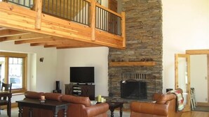 A spacious living room with a stone fireplace, wooden ceiling beams, and a television. - Golf Course/Lodge Style/large/clean/comfortable/5 BR (Black Butte Ranch)