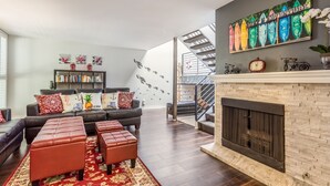 A modern living room with a fireplace, a staircase, and a bookshelf. - Spacious Beach House (Solana Beach)