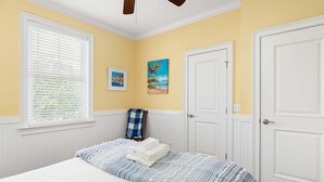 Een slaapkamer met een bed, een raam met zonwering, een deur en twee schilderijen aan de muur.