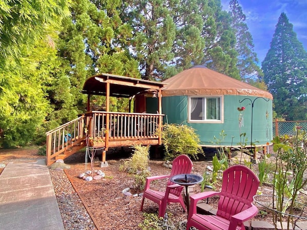 A small cabin with a deck, surrounded by trees.