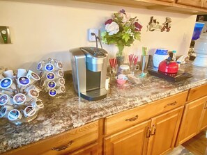 A kitchen counter with a coffee maker, a jar of coffee pods, a vase with flowers, and a red kettle.