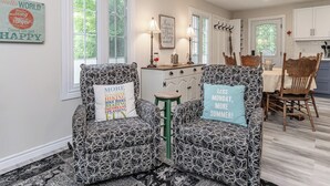 A cozy living room with patterned chairs, a small table, and a kitchen in the background. - 4 Season Cottage at Lake Vernon - Perfect for families! (Huntsville)