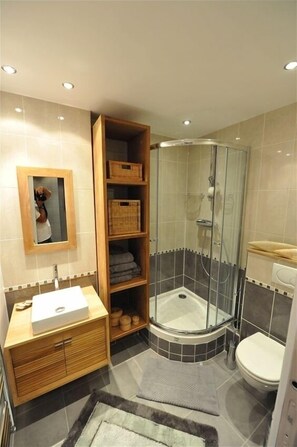A modern bathroom with a glass-enclosed shower, a wooden vanity, and a built-in shelf with baskets. - Perfect Location to Visit All of Paris - Contemporary Cozy (Paris)