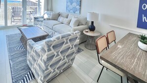 Ein modernes Wohnzimmer mit einer Couch, einem Couchtisch und einem Esstisch. Durch große Fenster ist der Blick aufs Meer möglich.