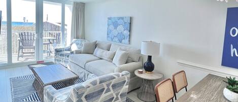 A modern living room with a sofa, coffee table, and dining table. There is a view of the ocean through large windows.