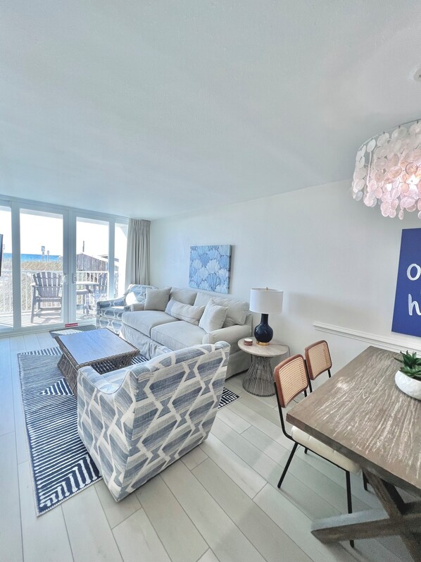 A modern living room with a sofa, coffee table, and dining table. There is a view of the ocean through large windows.