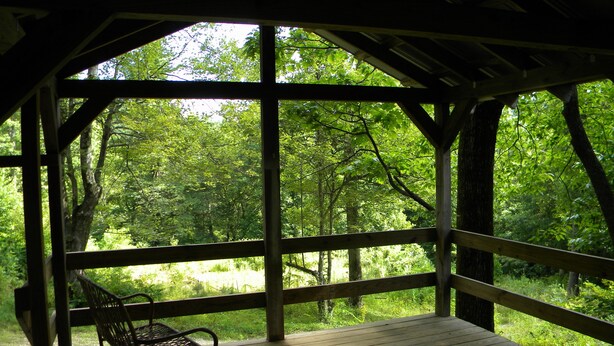 A covered wooden deck with a bench, surrounded by trees.