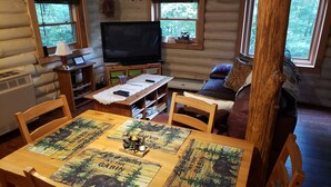 A cozy cabin interior with a wooden dining table, chairs, a television, and a sofa.