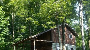 A rustic cabin with a wooden deck and stairs leading to a windowed porch.