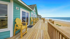 Eine Holzterrasse mit Stühlen, einer Glastür und Blick auf den Strand.