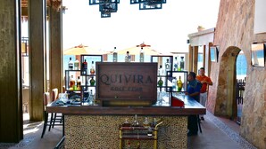 A bar area with a sign reading "QUIVIRA GOLF CLUB," a display of liquor bottles, and a seating area with chairs and tables. - 4966sf Penthouse Great Ocean Views +25% Off Golf (Los Cabos, Cabo San Lucas Centro)