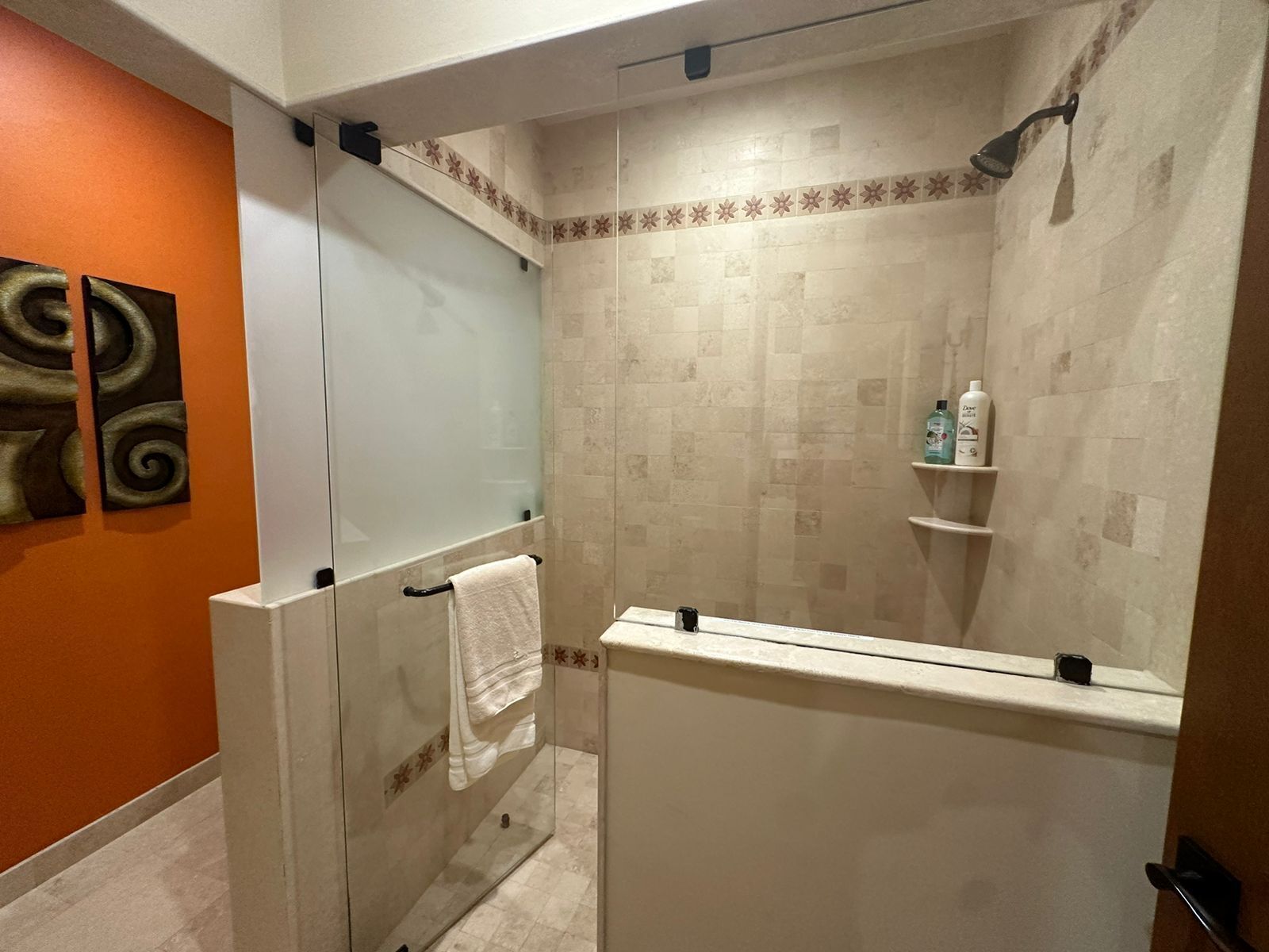 Une salle de bain avec une douche à parois de verre, un lavabo blanc et un miroir. On y trouve deux étagères avec des articles de toilette.
