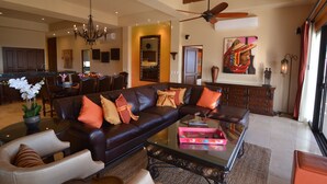 A spacious living room with a dark leather sofa, a glass coffee table, and a dining area in the background. - 4966sf Penthouse Great Ocean Views +25% Off Golf (Los Cabos, Cabo San Lucas Centro)