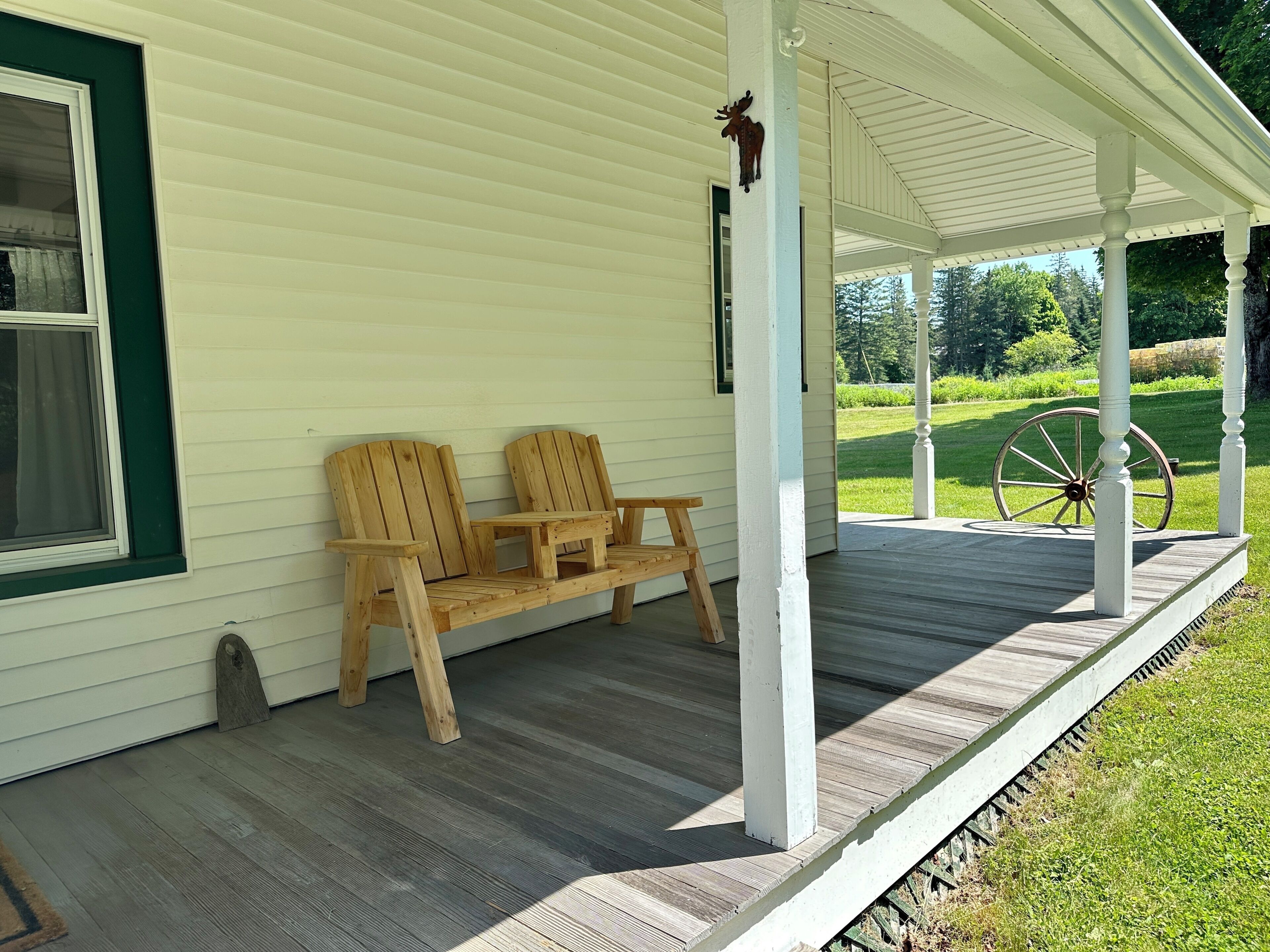 A wooden porch with two chairs and a bench, a white railing, and a green window frame.