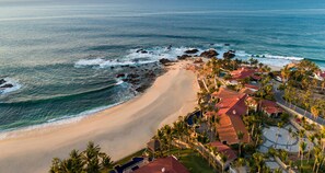 A coastal property with a sandy beach, a swimming pool, and a red-roofed building.
