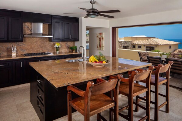 A kitchen with dark cabinets, a granite countertop, a built-in stove, and a large island with bar stools.