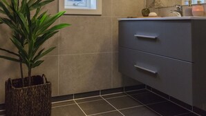Un baño con ventana, planta en maceta, lavabo y espejo.