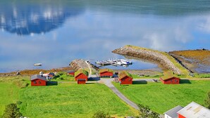 Un pueblo costero con casas rojas, un muelle y una gran formación rocosa.