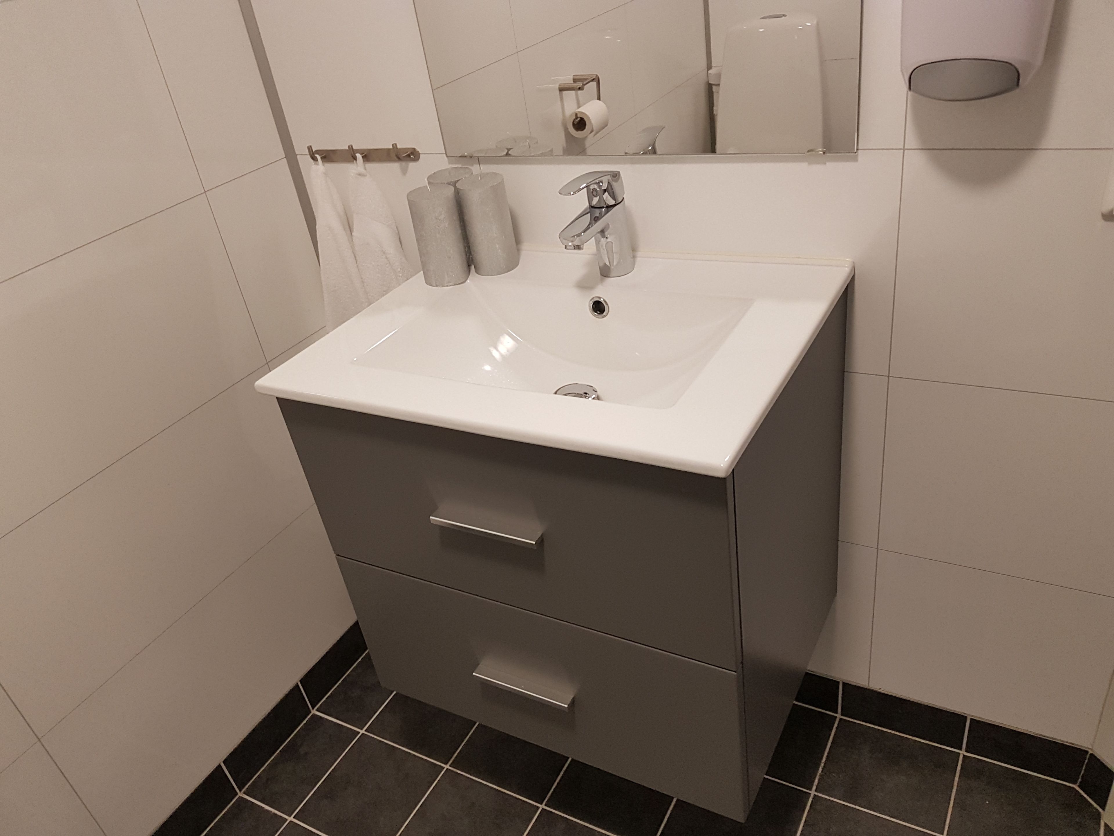 A bathroom with a white sink, a mirror, and a toilet paper holder.