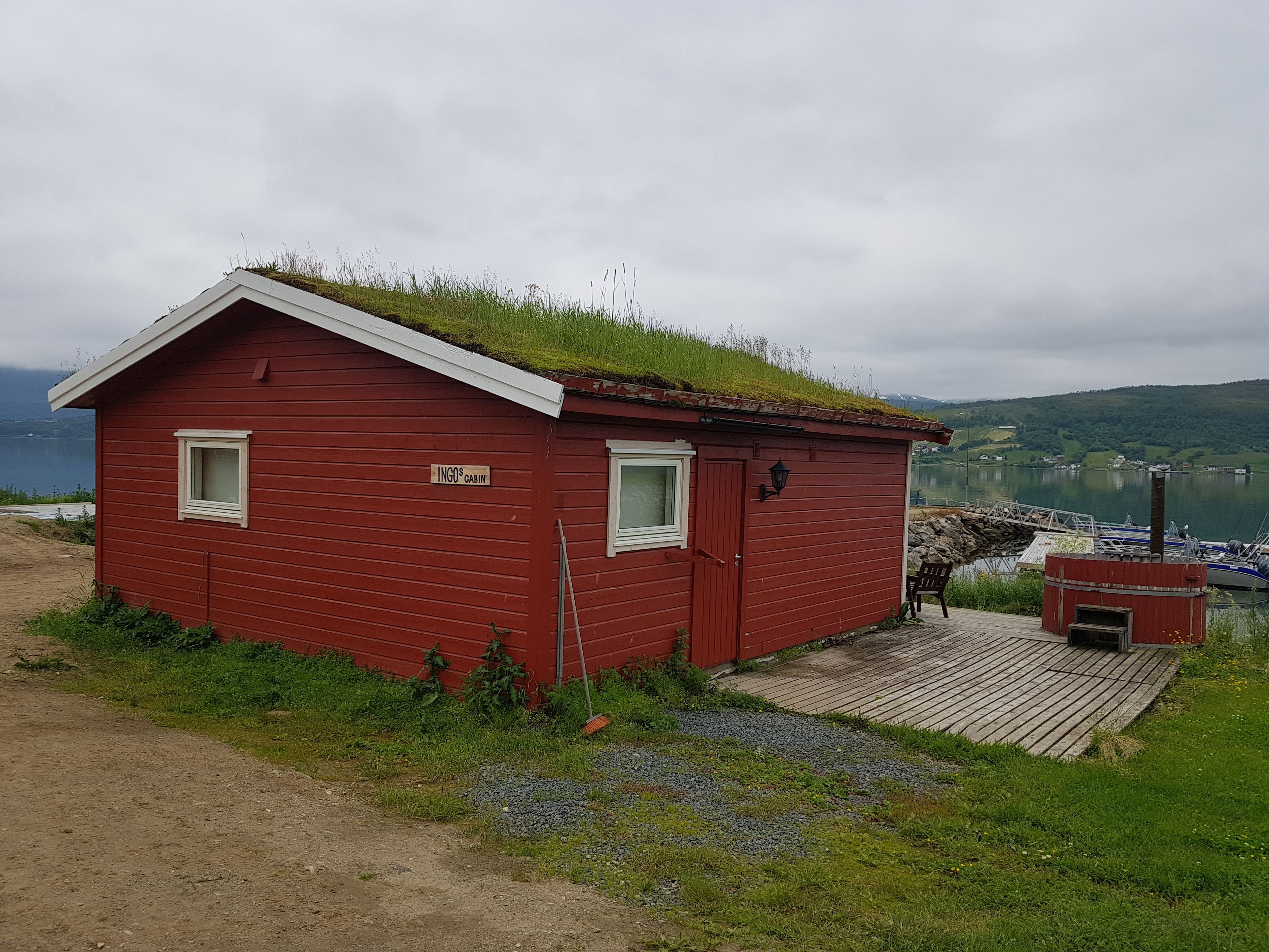 A red cabin with a grass roof, a sign reading "INGO'S CABIN," and a dock with boats.