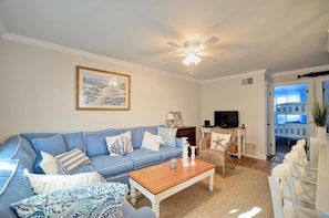 A living room with a blue sofa, a wooden coffee table, and a ceiling fan. - Great Condo in North Bethany, steps from the Beach! (Bethany Beach)