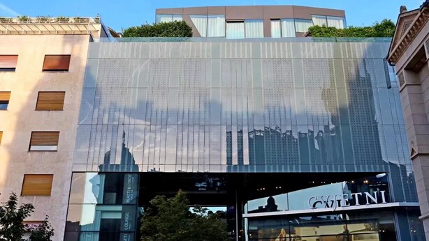 Un bâtiment moderne doté d’une façade en verre qui reflète le paysage urbain, d’un jardin sur le toit et d’une enseigne de restaurant bien visible.