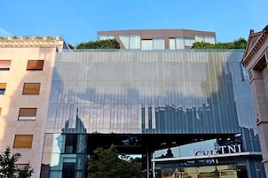 Un edificio moderno con fachada de vidrio que refleja el horizonte urbano, un jardín en la azotea y un letrero de restaurante a la vista.