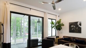 Un salon moderne comprenant un canapé, une table à manger et une grande fenêtre donnant sur la nature et les arbres.