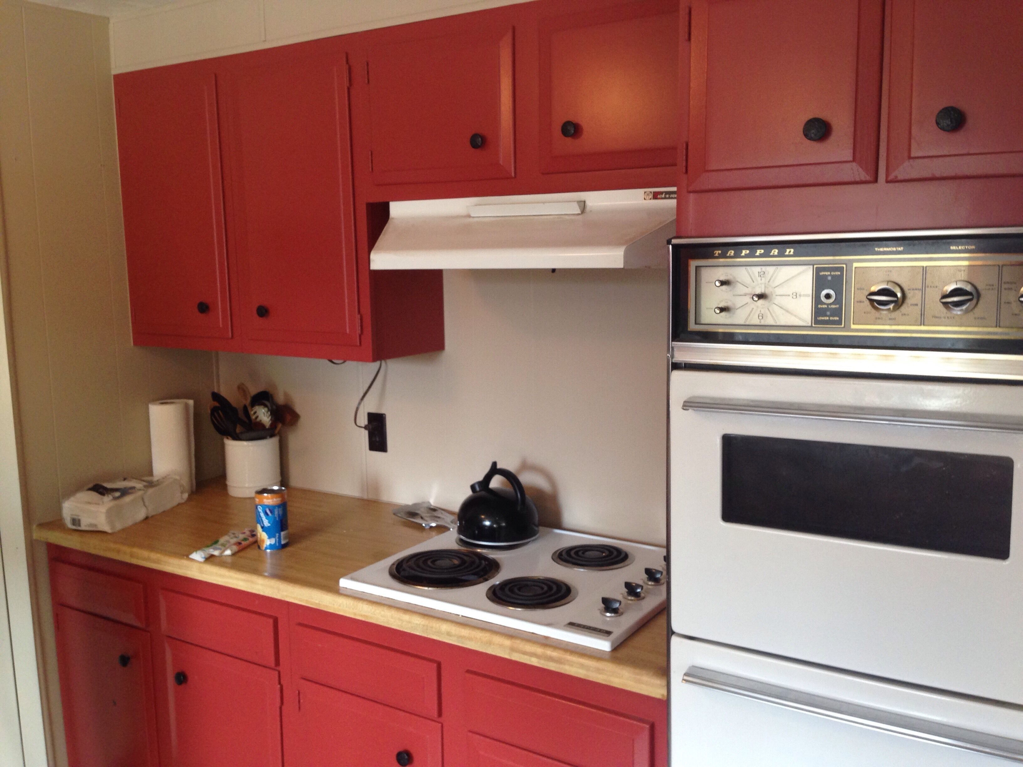A kitchen with red cabinets, a white stove, and a black kettle on the counter.