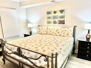 A bedroom with a bed, bedside tables, a wall-mounted artwork, and a window with blinds.