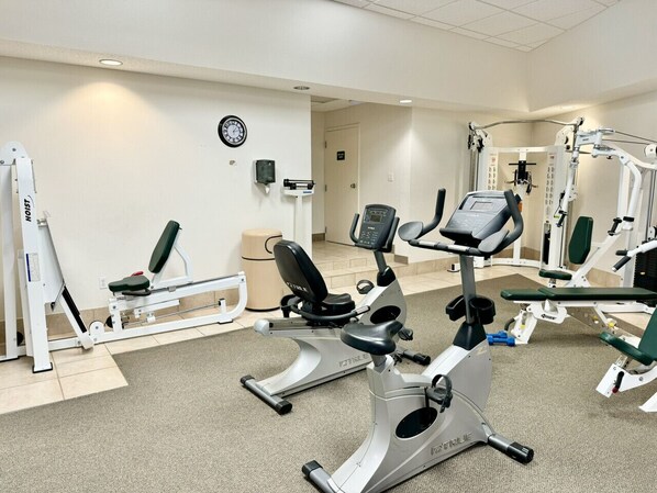 A gym with cardio machines, weight stations, and a wall clock.