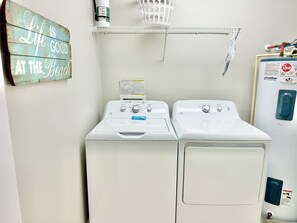 A laundry room with two front-loading washing machines, a wall-mounted shelf, and a sign that reads "Life is good at the beach".