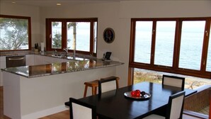 Uma cozinha moderna com uma ilha central, grandes janelas com vista para o mar e uma área de jantar com mesa e cadeiras.