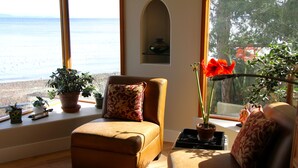 Uma sala de estar acolhedora com vista para a praia, apresentando um sofá marrom, uma mesinha e algumas plantas em vasos.