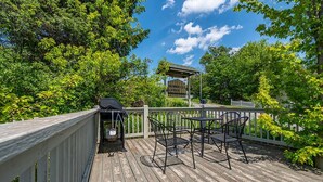 A wooden deck with outdoor seating, surrounded by lush greenery and a clear blue sky.