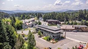 A small town with a mix of residential and commercial buildings, surrounded by dense forests and mountains in the background.
