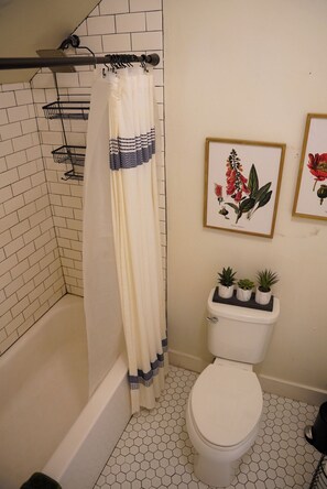 Un bagno con tenda doccia, un water e due stampe botaniche incorniciate al muro.