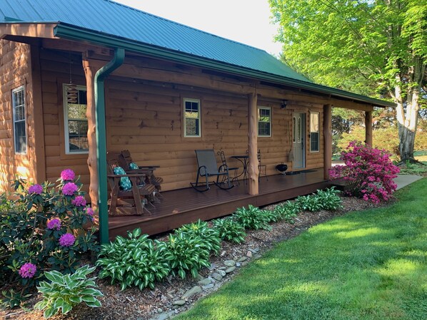 A log cabin with a porch, outdoor seating, and a garden with flowers and shrubs. - Lazy Lake Cabins - Cozy comfort in the Blue Ridge Mountains (Hendersonville)