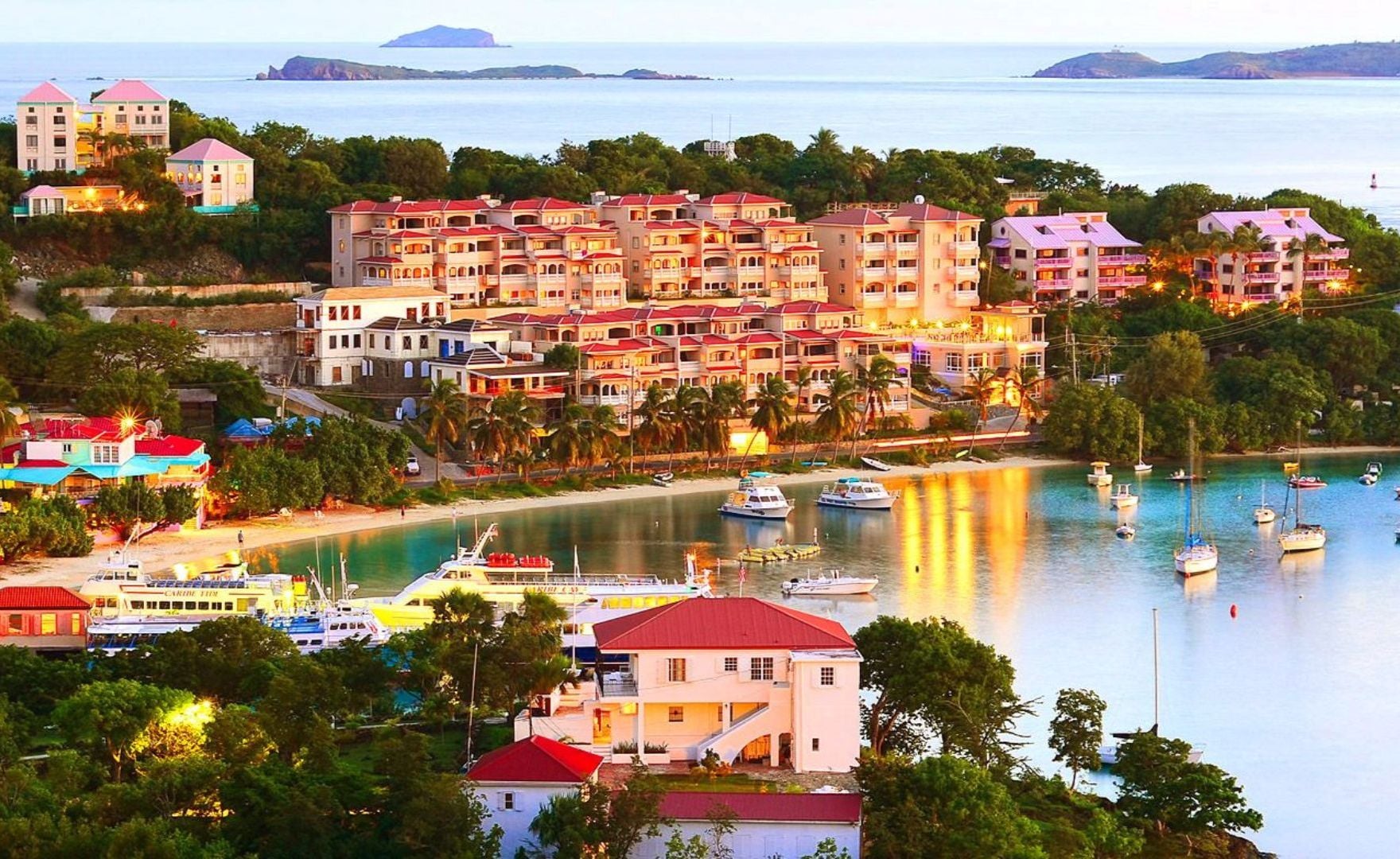 A coastal resort with multiple buildings, a marina with boats, and a view of the sea and distant islands.
