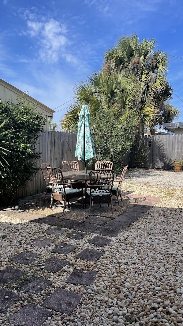 An outdoor patio with a table and chairs, surrounded by a wooden fence and palm trees.