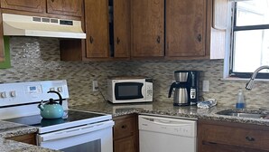 Una cocina con encimeras de granito, gabinetes de madera, estufa, microondas y lavavajillas.