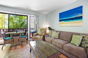 A living room with a sofa, armchairs, a coffee table, and a dining area with a table and chairs. There is a large window with a view of greenery outside. - LOW Summer rates -Free parking/no resort fees A/C (Kihei)