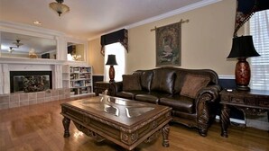 A living room with a fireplace, leather sofa, wooden coffee table, and a bookshelf. - Granbury's  Luxurious  'Abbey Manor'. Walk to Historic Square (Granbury)